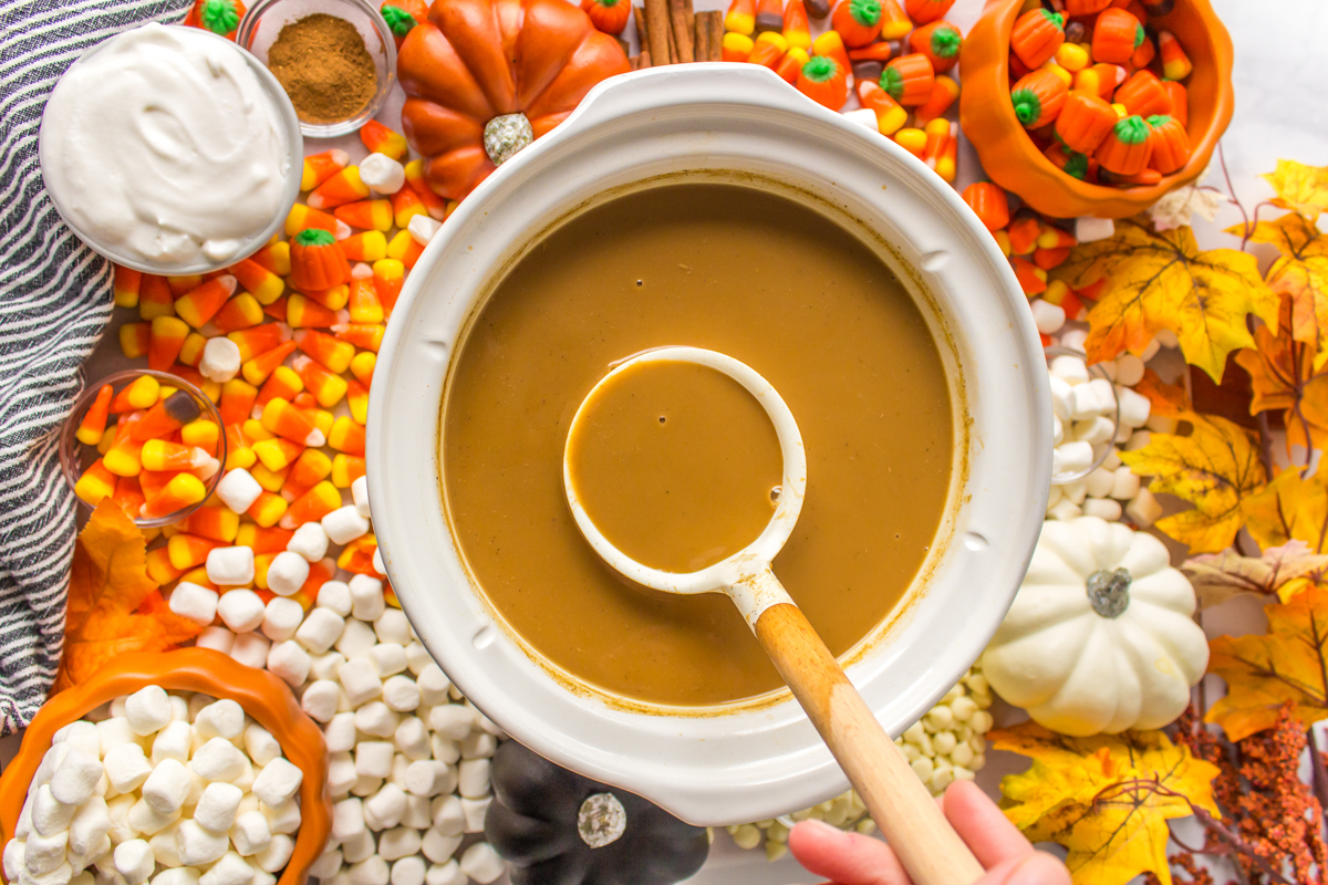 overhead shot of pumpkin spice lattes in a slow cooker with candies around it.