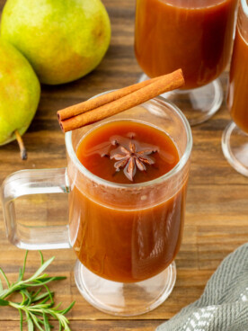 pear cider in a clear mug with cinnamon stick on top.