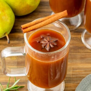 pear cider in a clear mug with cinnamon stick on top.