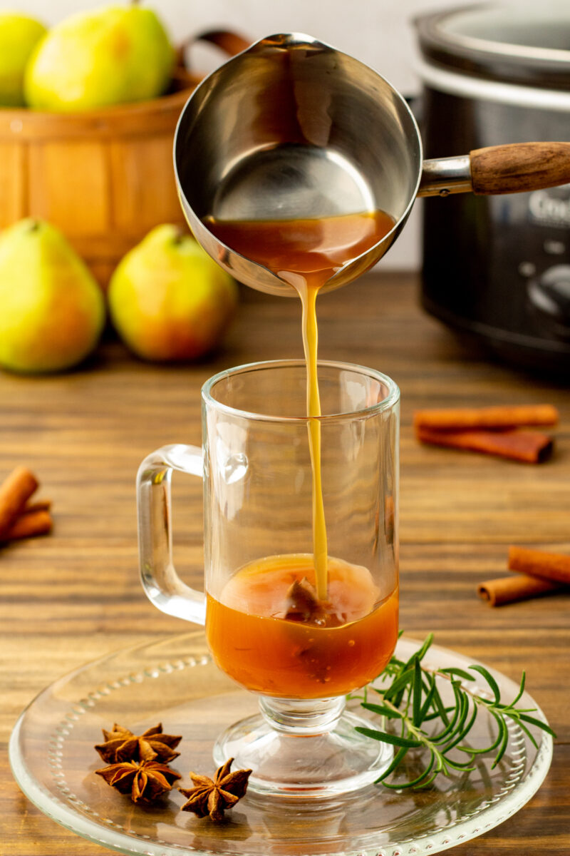 pear cider being pour into a mug in front of a slow cooker.