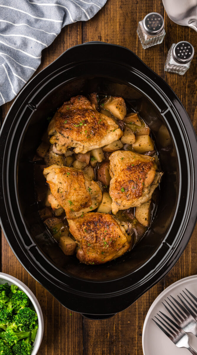 Long image of chicken thighs and potatoes in a slow cooker.