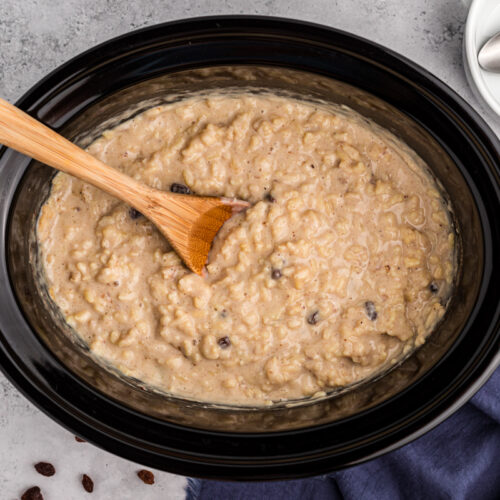 Rice pudding in a crockpot with a wooden spoon in it.