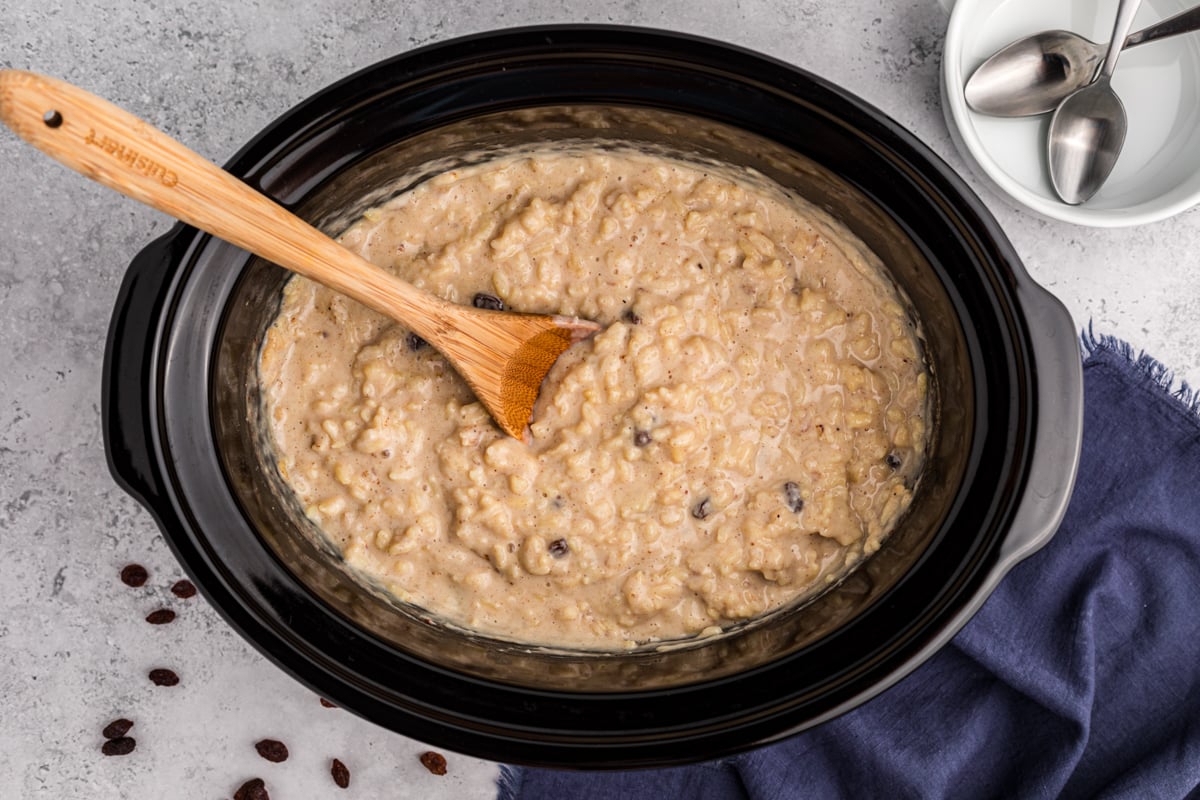 Rice pudding in a crockpot with a wooden spoon in it.