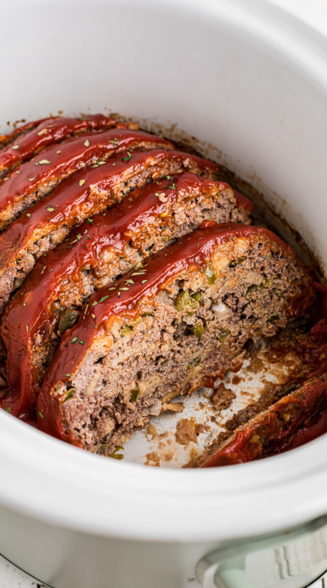 sliced meatloaf with a glaze in a white slow cooker.