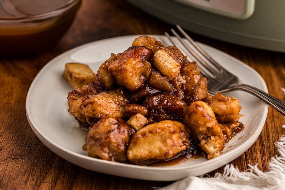 close-up of slow cooker caramel apple cinnamon roll casserole on a plate with a fork.