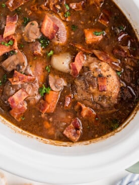 overhead shot of coq au vin in a white slow cooker.