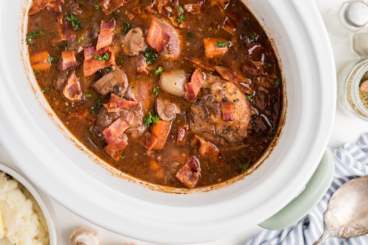 overhead shot of coq au vin in a white slow cooker.