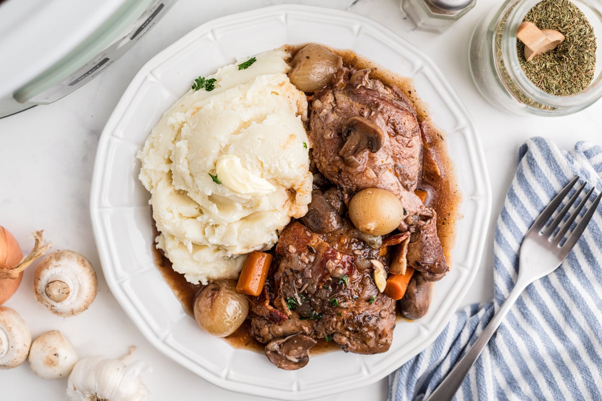 overhead shot of crockpot coq au vin with mashed potatoes on a white plate.
