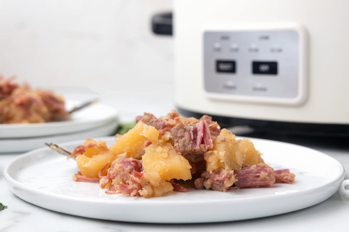 Plate of corned beef and cabbage in front of a slow cooker.