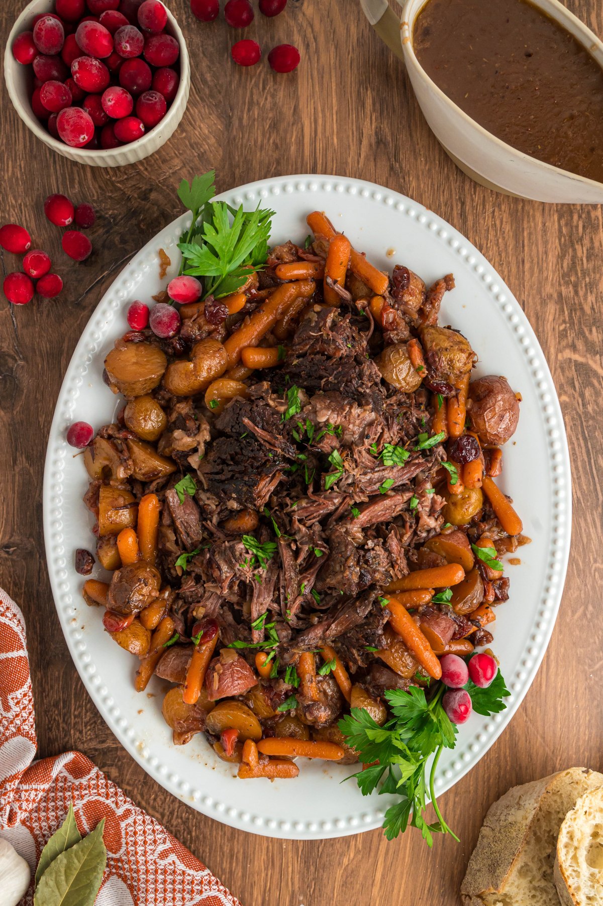 Pot roast on a platter with veggies and cranberries.