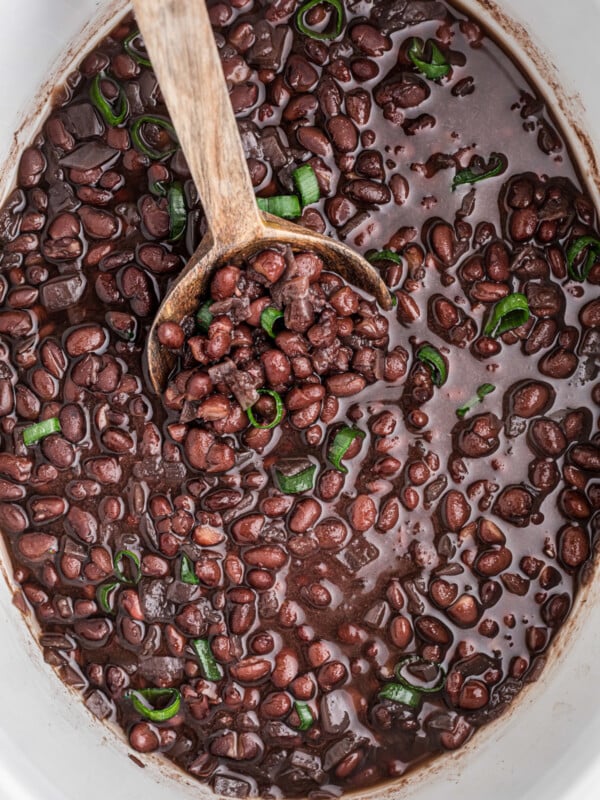 black beans in a slow cooker with a wooden spoon.
