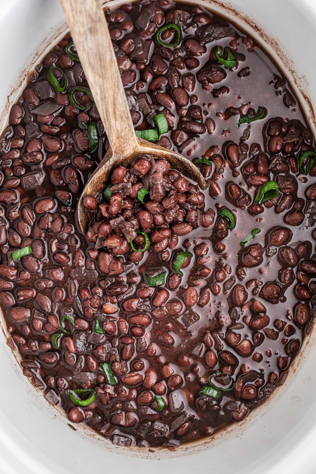 black beans in a slow cooker with a wooden spoon.