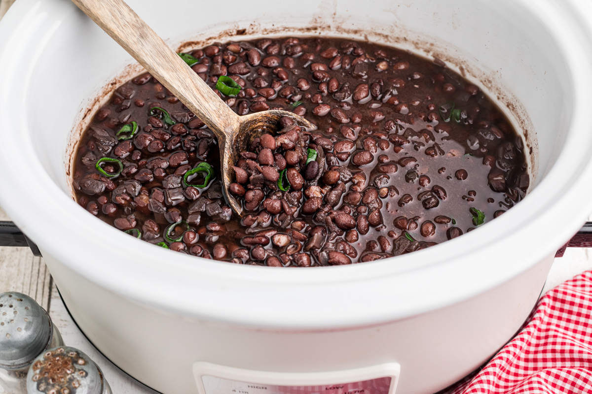 black beans, done cooking in a slow cooker with a wooden spoon in it.