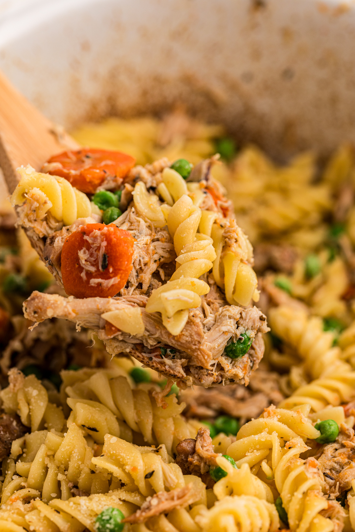 scooping garlic butter chicken and pasta out of a crockpot.