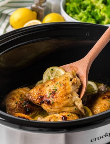 scooping out some lemon pepper chicken thighs from a crockpot with a wooden spoon.
