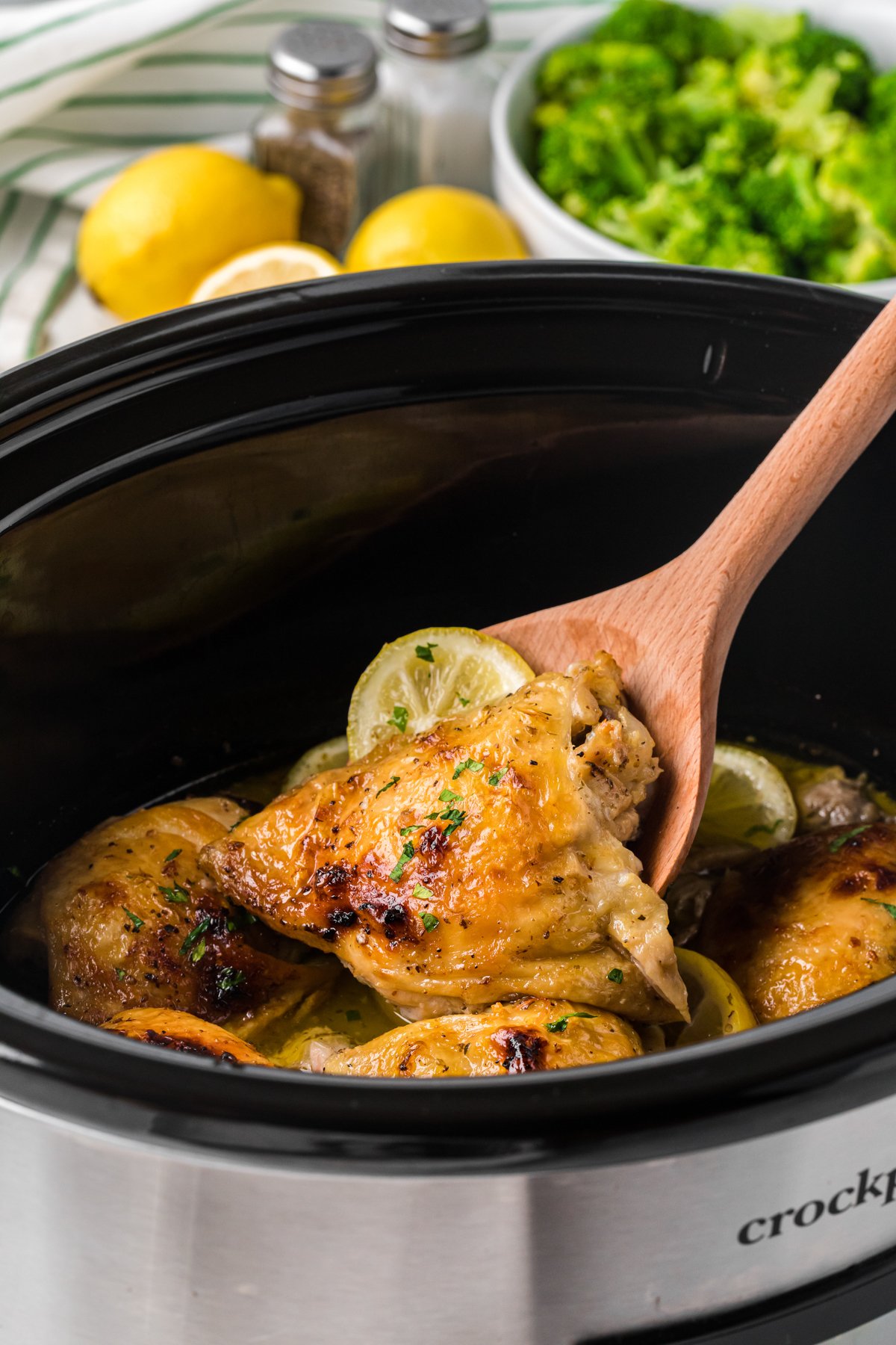 scooping out some lemon pepper chicken thighs from a crockpot with a wooden spoon.