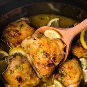 lemon pepper chicken thighs in a crockpot with a wooden spoon in it.