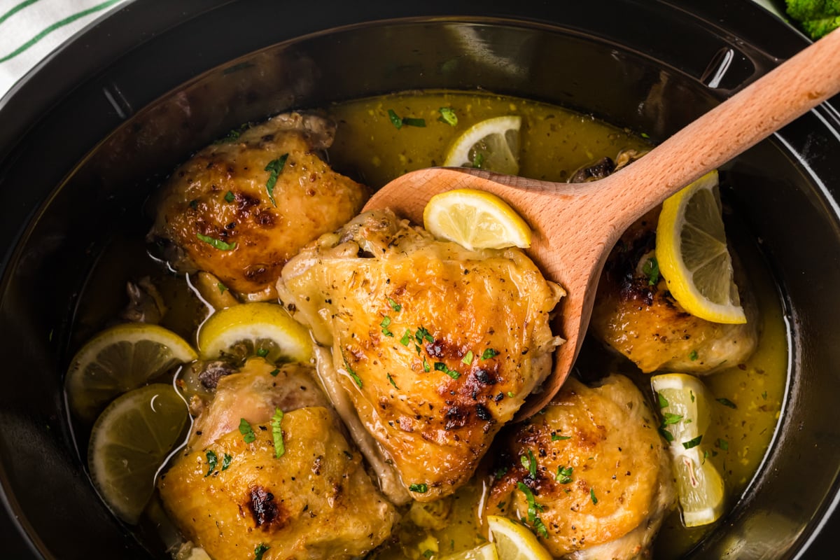 lemon pepper chicken thighs in a crockpot with a wooden spoon in it.