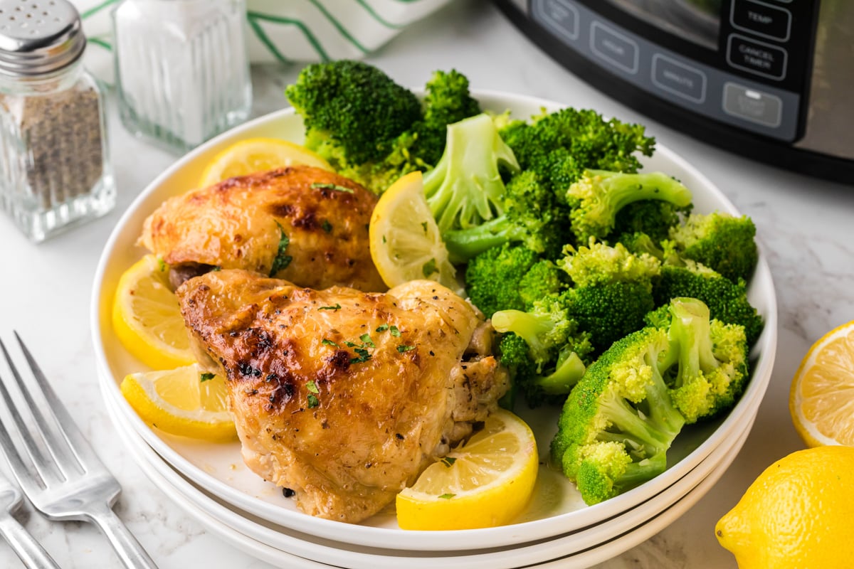 serving of slow cooker lemon pepper chicken thighs on stack of white plates.