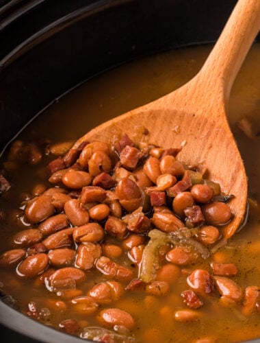 Pinto beans and ham in a slow cooker with wooden spoon.