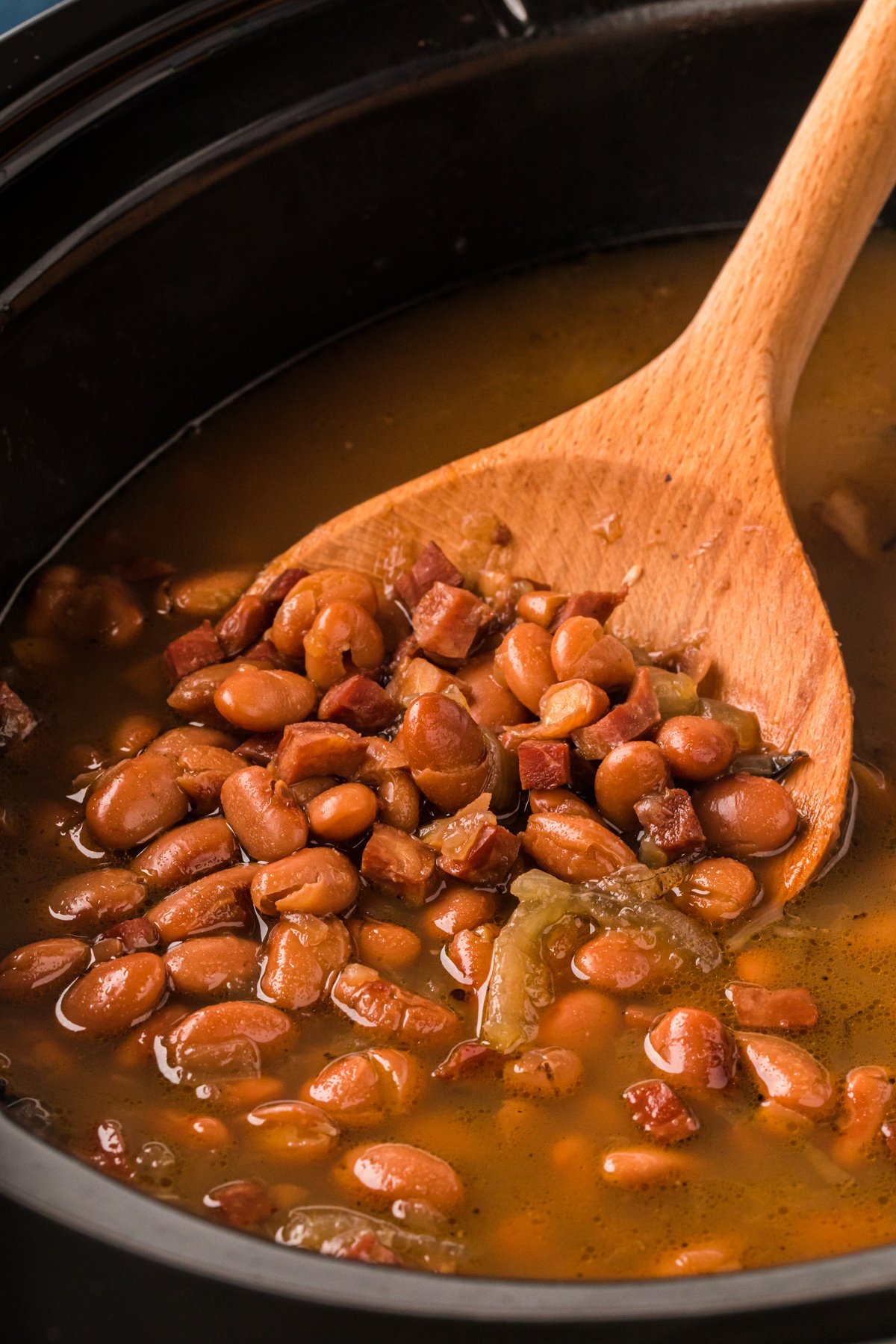 Pinto beans and ham in a slow cooker with wooden spoon.