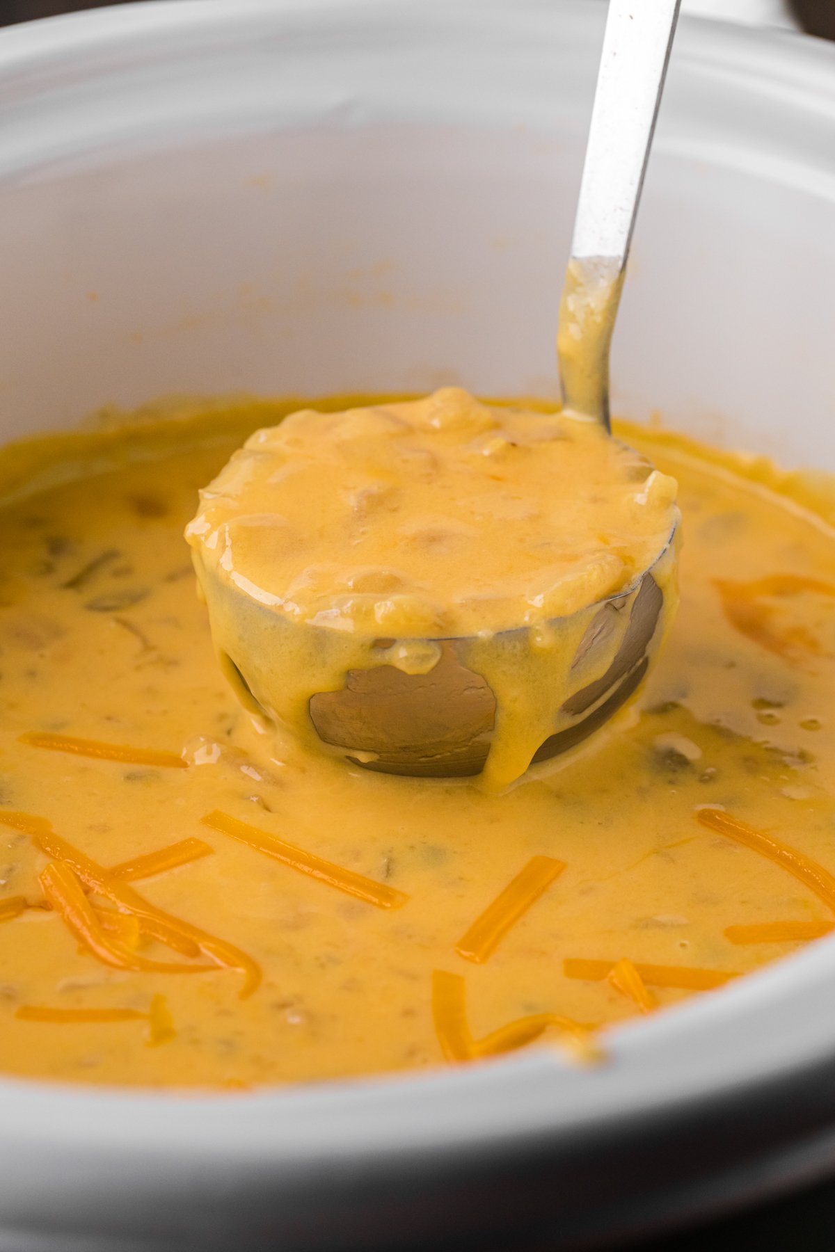 Potato cheese soup on a ladle coming from a crockpot.