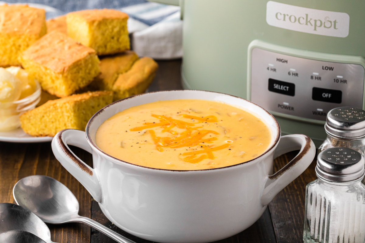 Bowl of potato cheese soup with crockpot in the background.