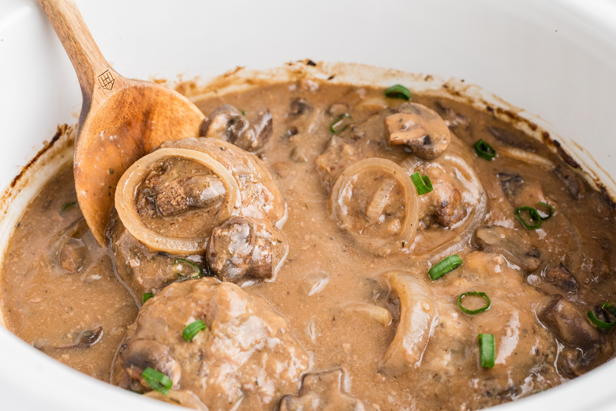 cooked salisbury steak in a slow cooker with a spoon in it.