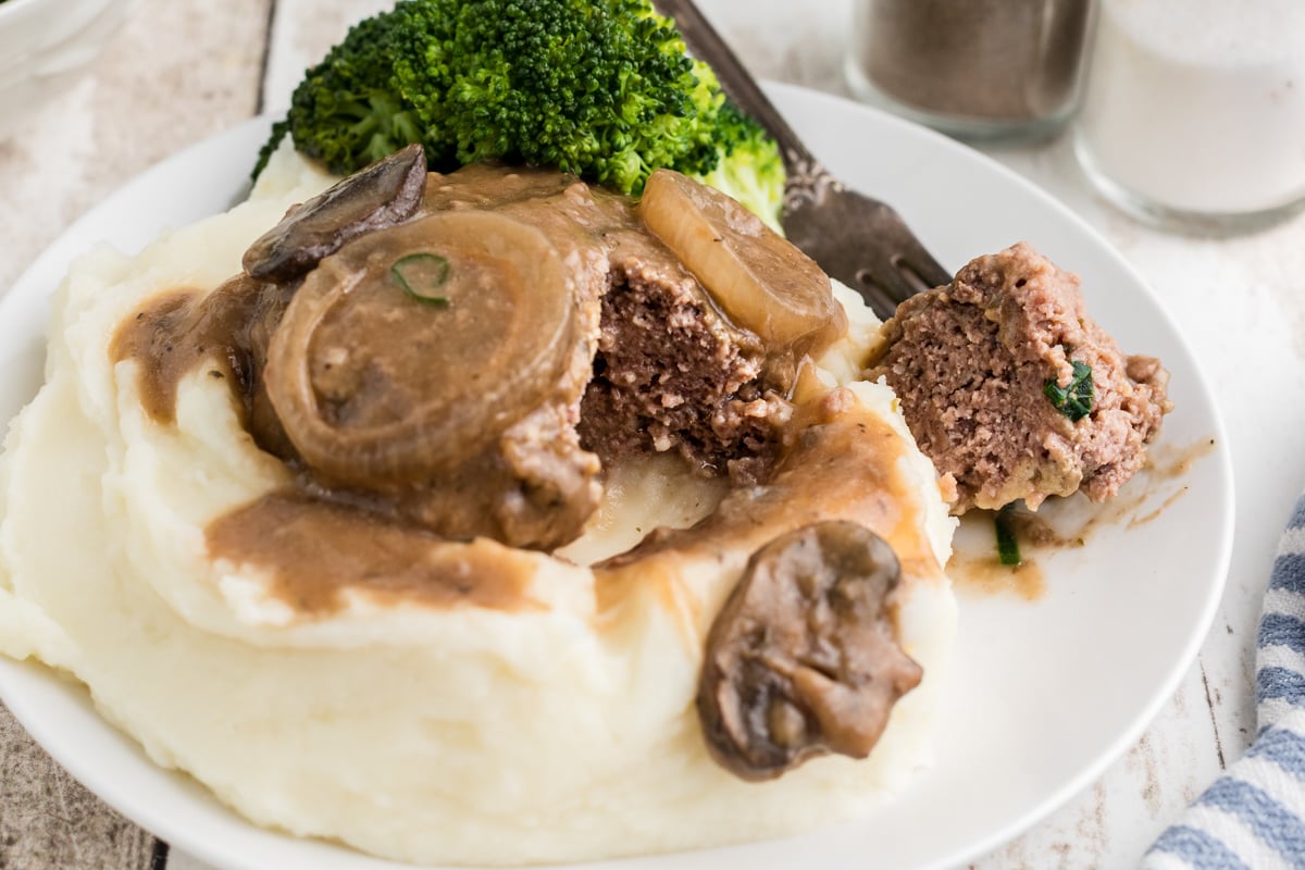 salisbury steak on a plate over mashed potatoes.