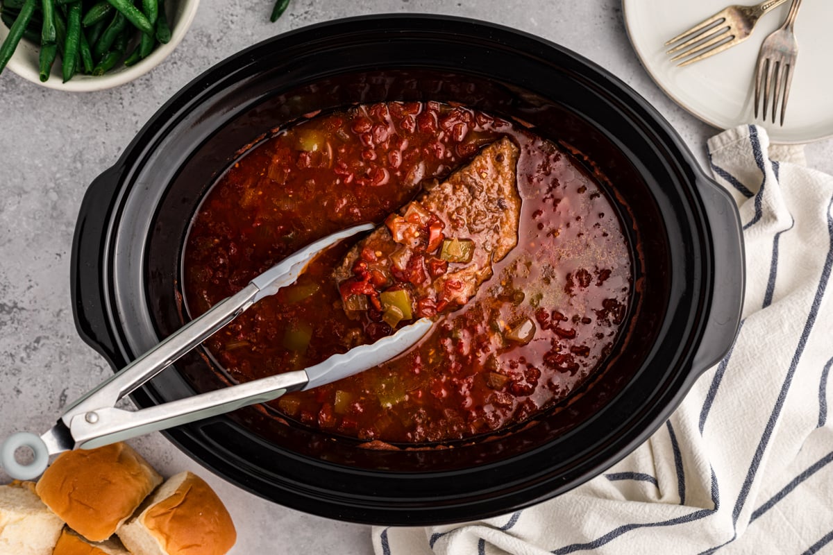 a piece of slow cooker swiss steak being held by tongs.