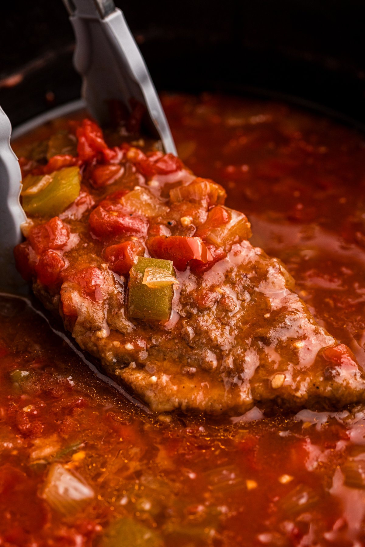 close-up of piece of swiss steak coming out of the crockpot.