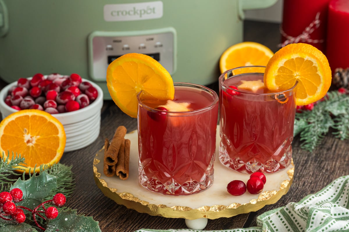 2 cups of warm christmas punch in front of a slow cooker.