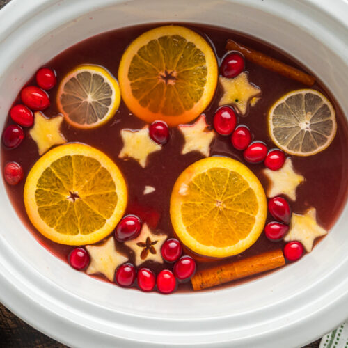 Red punch with lots of fruit in it in a slow cooker.