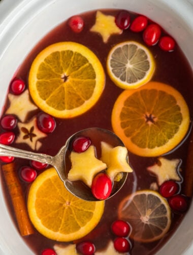 chrismtas punch in a slow cooker with apples shaped as stars and cranberries.