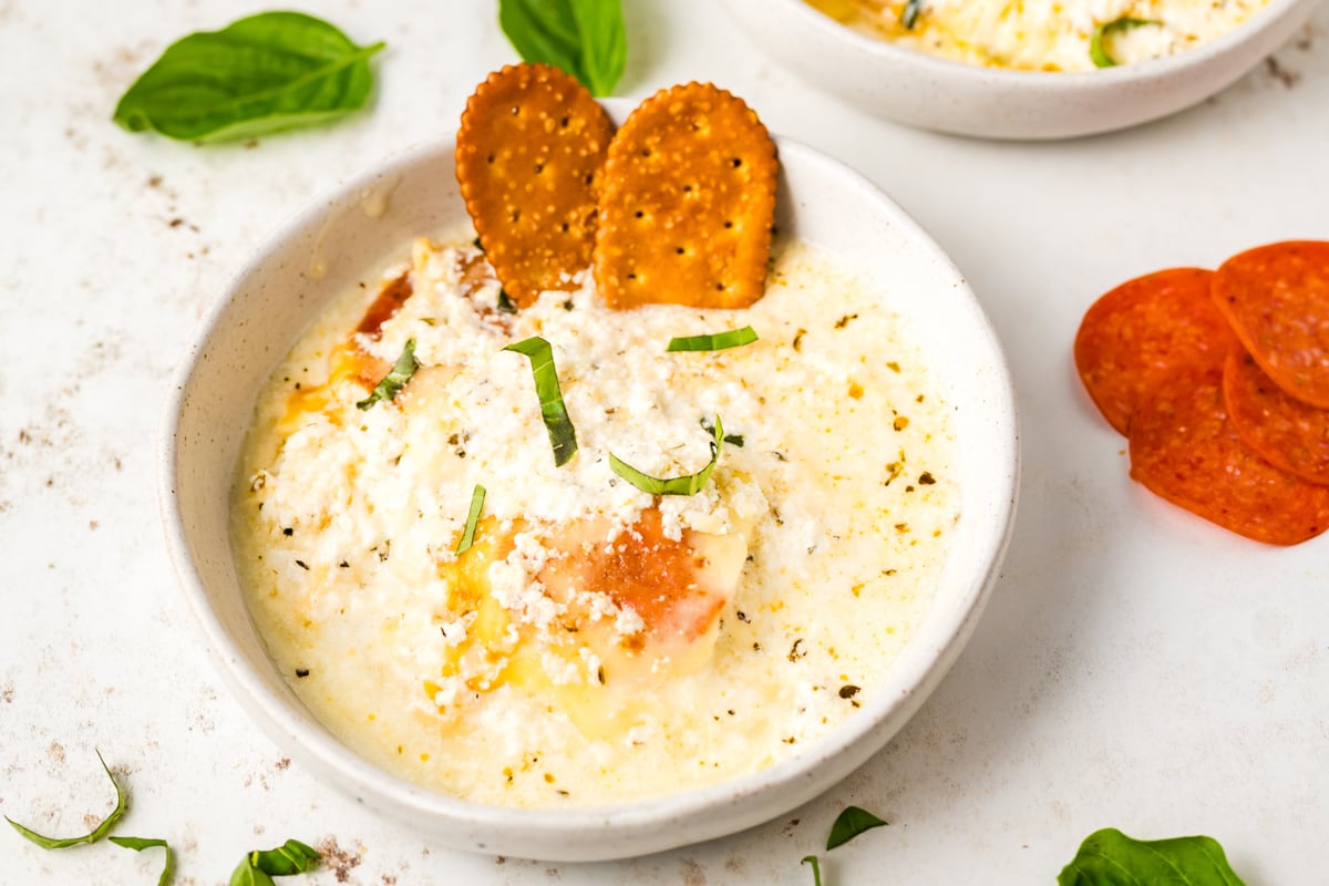 slow cooker white pizza dip in a white serving bowl with crackers.
