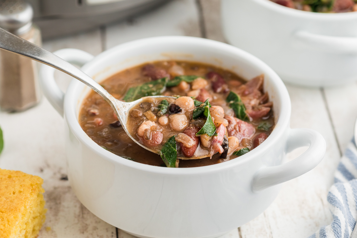 slow cooker 15 bean soup with ham and collard greens in a bowl with a spoon.