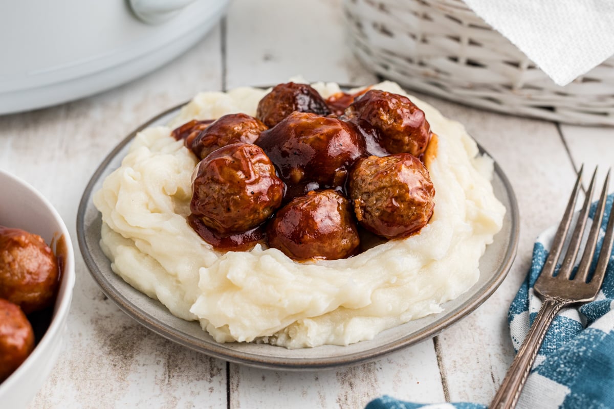 serving of slow cooker bbq meatballs on top of mashed potatoes on a plate.