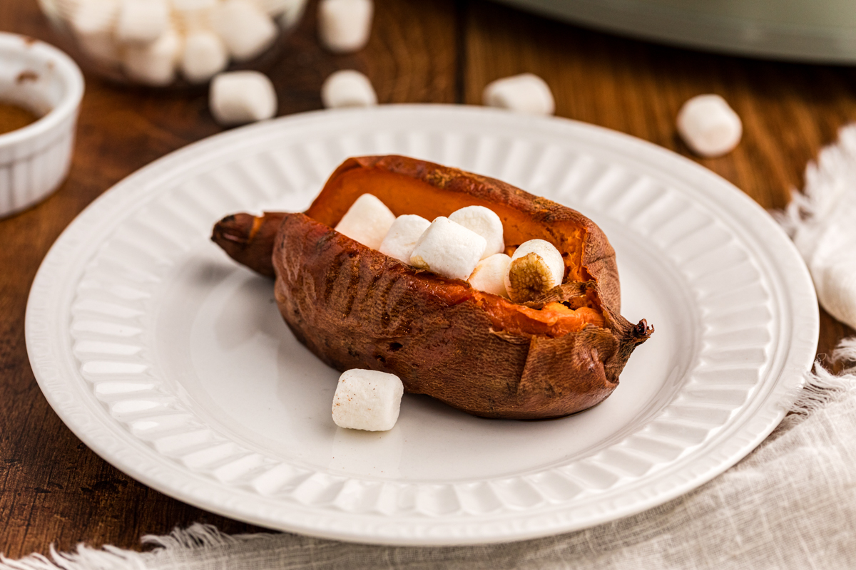 one of the slow cooker baked sweet potatoes on a white plate.