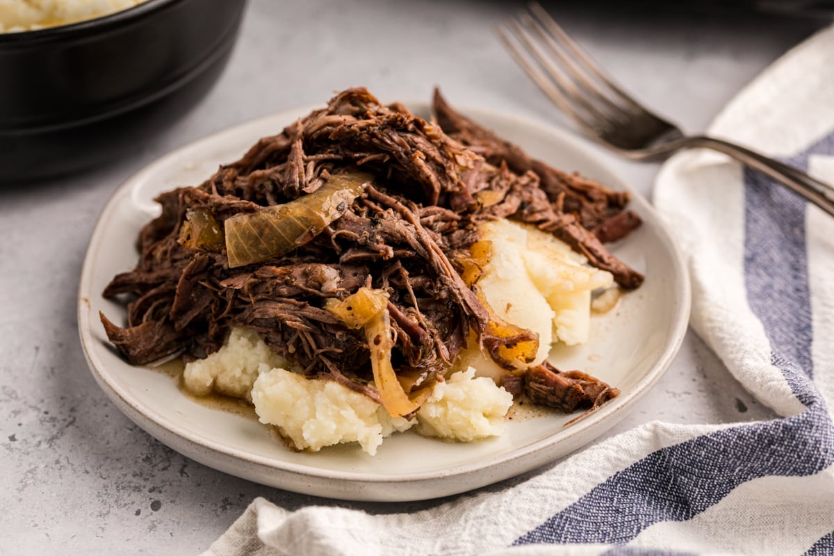 slow cooker balsamic beef on top of mashed potatoes on a white plate.