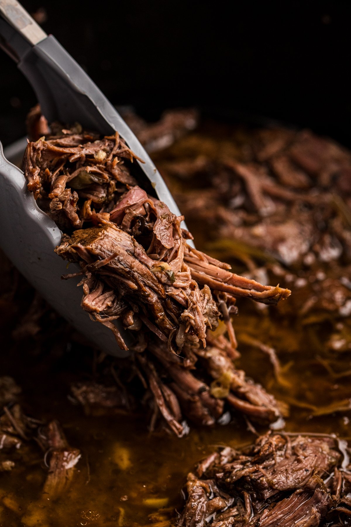 tongs pulling balsamic beef from a slow cooker.