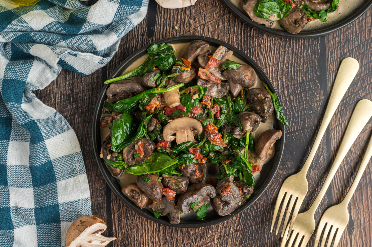 overhead of creamy tuscan mushrooms in a black serving dish.