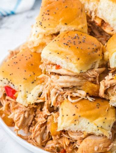 slow cooker Hawaiian sliders stacked on top of each other on a white plate.