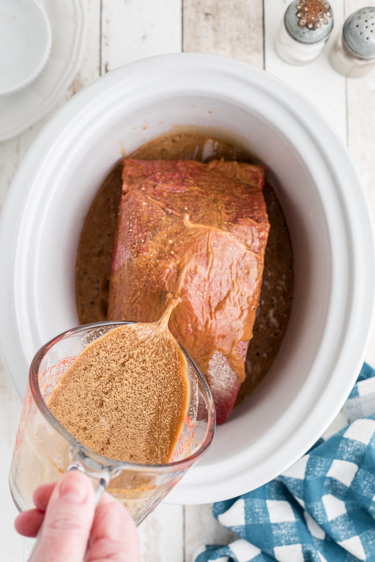 gravy mix being poured over roast in slow cooker.