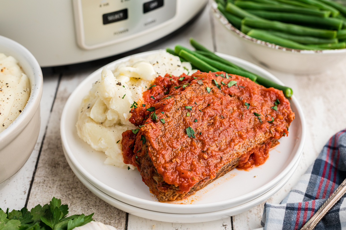 serving of Italian meatloaf with mashed potatoes and green beans on a white plate.