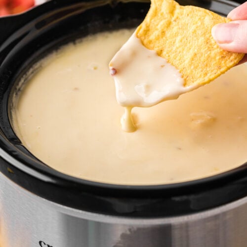 dipping a tortilla chip into restaurant style queso in a slow cooker.