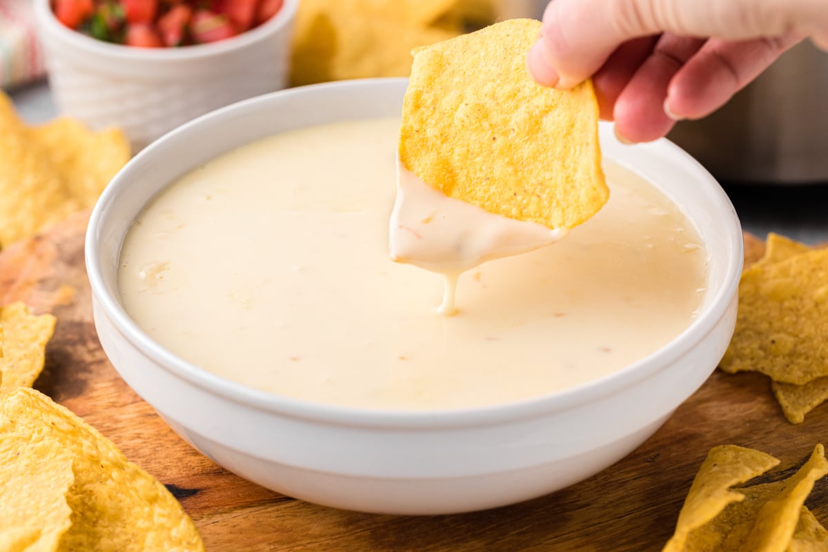 dipping a tortilla chip into a bowl of slow cooker restaurant style queso.