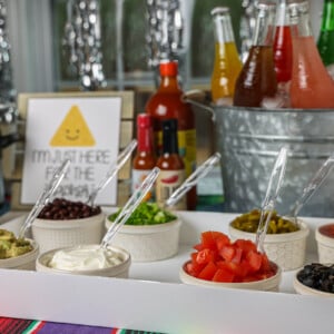 Ingredients for a nacho bar with drinks in the background.