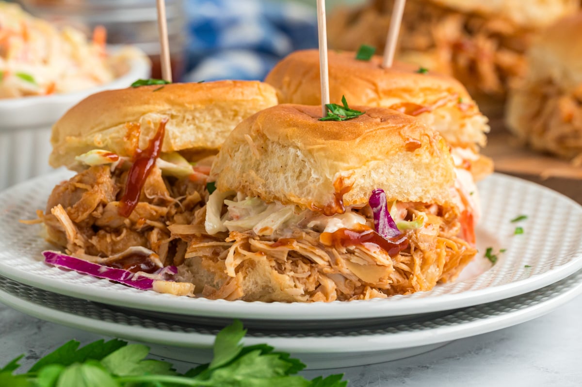 three slow cooker bbq chicken sliders on a stack of white plates.