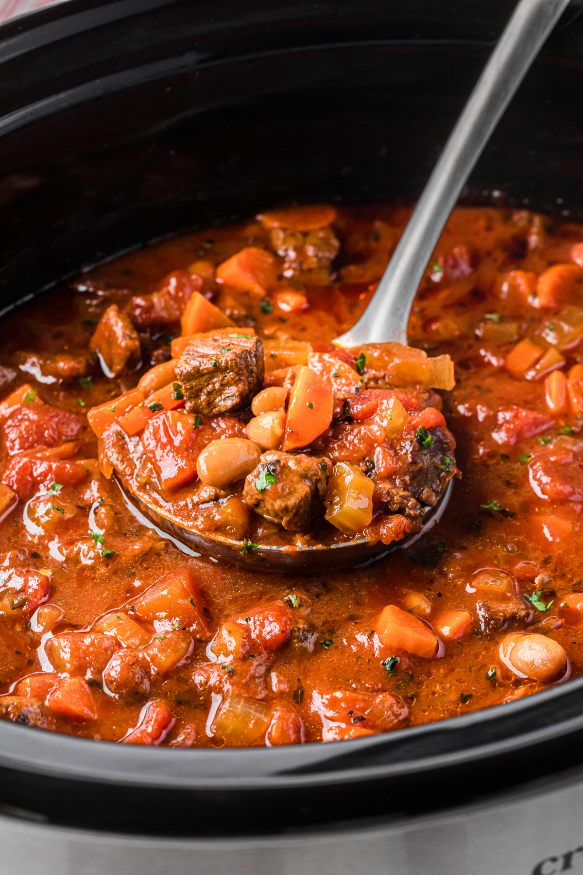 scooping hearty italian beef soup out of a slow cooker.