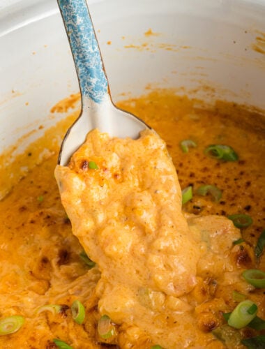 scooping hot shrimp dip out of slow cooker with a spoon.